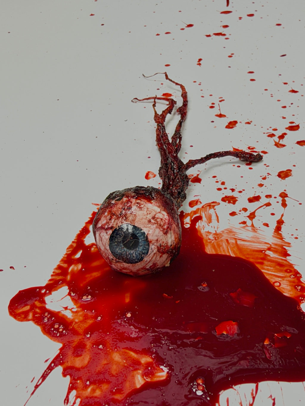 Front view of the handmade severed eyeball Halloween prop with a blue iris and bloody optic nerve