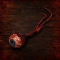 Handmade gory severed eyeball prop with a blue iris and attached optic nerve on dark wood